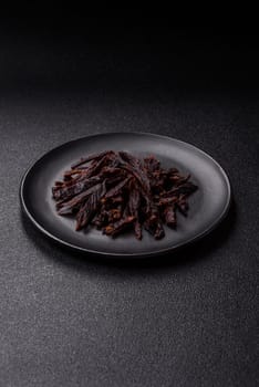 Jerky, dried horse meat or beef slices with salt and spices on a dark concrete background
