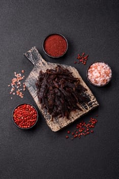 Jerky, dried horse meat or beef slices with salt and spices on a dark concrete background