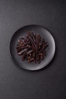 Jerky, dried horse meat or beef slices with salt and spices on a dark concrete background