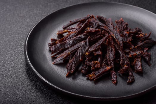 Jerky, dried horse meat or beef slices with salt and spices on a dark concrete background