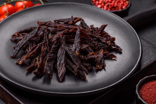 Jerky, dried horse meat or beef slices with salt and spices on a dark concrete background