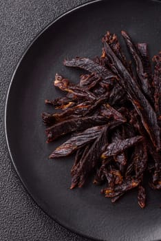 Jerky, dried horse meat or beef slices with salt and spices on a dark concrete background