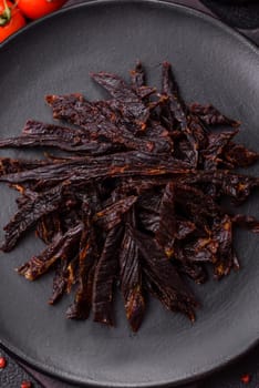Jerky, dried horse meat or beef slices with salt and spices on a dark concrete background