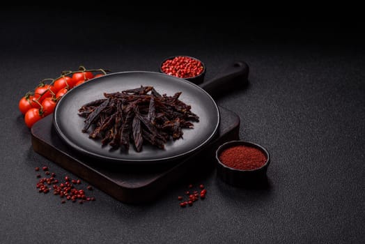 Jerky, dried horse meat or beef slices with salt and spices on a dark concrete background