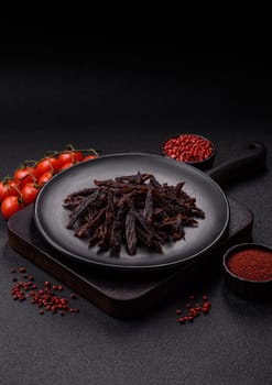 Jerky, dried horse meat or beef slices with salt and spices on a dark concrete background