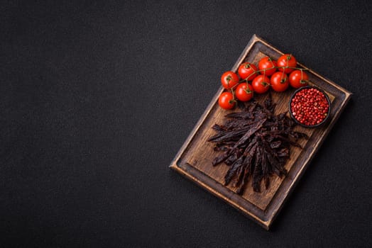 Jerky, dried horse meat or beef slices with salt and spices on a dark concrete background