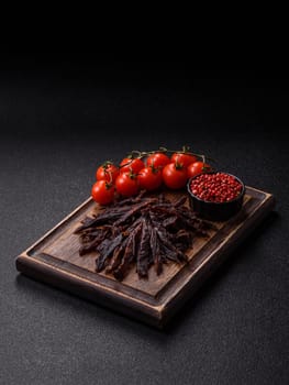 Jerky, dried horse meat or beef slices with salt and spices on a dark concrete background