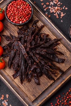 Jerky, dried horse meat or beef slices with salt and spices on a dark concrete background