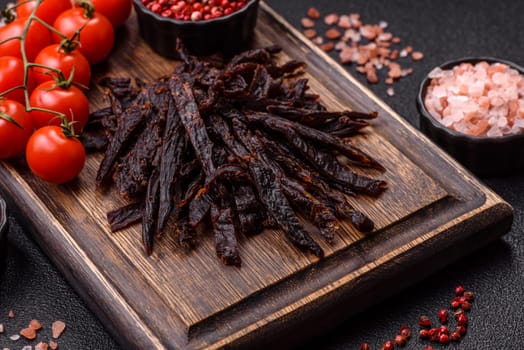 Jerky, dried horse meat or beef slices with salt and spices on a dark concrete background