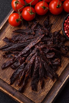Jerky, dried horse meat or beef slices with salt and spices on a dark concrete background