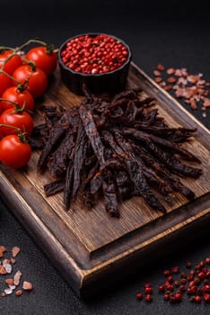 Jerky, dried horse meat or beef slices with salt and spices on a dark concrete background