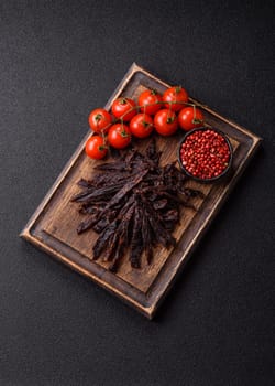 Jerky, dried horse meat or beef slices with salt and spices on a dark concrete background