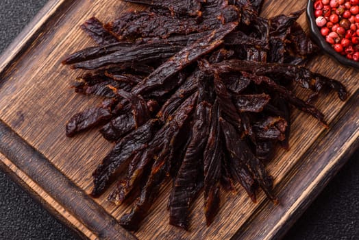 Jerky, dried horse meat or beef slices with salt and spices on a dark concrete background