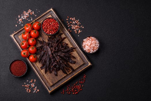 Jerky, dried horse meat or beef slices with salt and spices on a dark concrete background