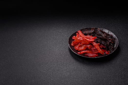 Jerky, dried chicken slices with salt and spices on a dark concrete background