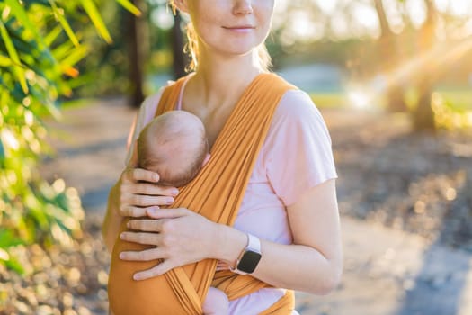 A loving mother walks through a peaceful park, carrying her baby securely in a sling. A heartwarming moment of maternal bonding, babywearing, and the joy of motherhood in nature.