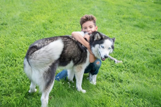 The boy is kneeling on the luscious green grass, hugging his affectionate Siberian Husky dog tightly after playing with a bone together on the green lawn, demonstrating their special bond,