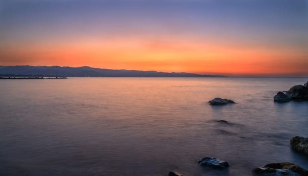 Golden and orange rays reflect on tranquil waves as the day comes to a peaceful close near the coastline.