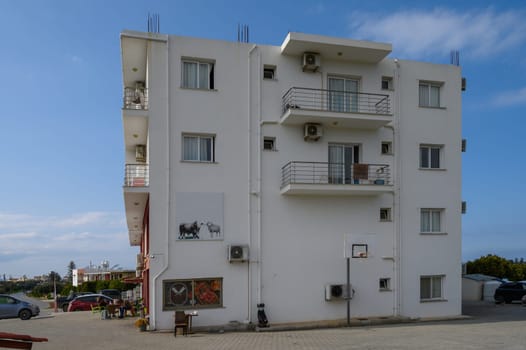 Bright white building features artistic mural and basketball hoop, surrounded by parked cars and clear sky.