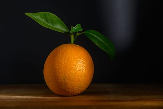 Bright orange sits on warm wood, showcasing its vibrant color and fresh leaves against a dark backdrop.