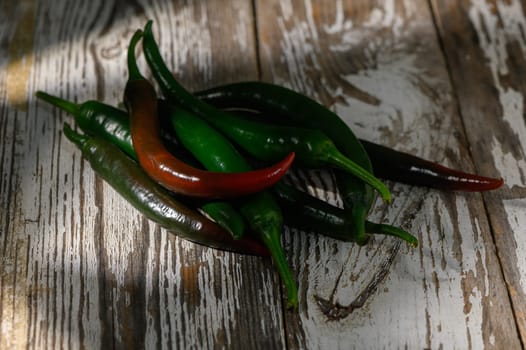 A colorful collection of green and red chilies contrasts beautifully on an aged wooden table, showcasing freshness.