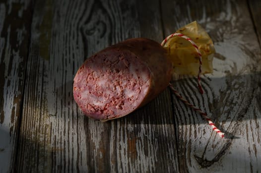 Savoring the artisanal flavors, a beautifully crafted sausage lies on a weathered wooden table, bathed in gentle light.