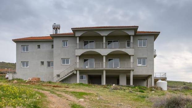 A spacious villa with arches and balconies, surrounded by green fields under a moody sky, showcases rustic charm.