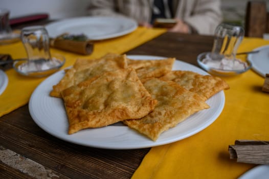Crispy, golden-brown pastries arranged on a white plate, inviting at a rustic dining setting with friends.