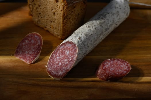 Slices of rich salami laid beside a crusty loaf of bread on a wooden board, showcasing inviting textures and colors.