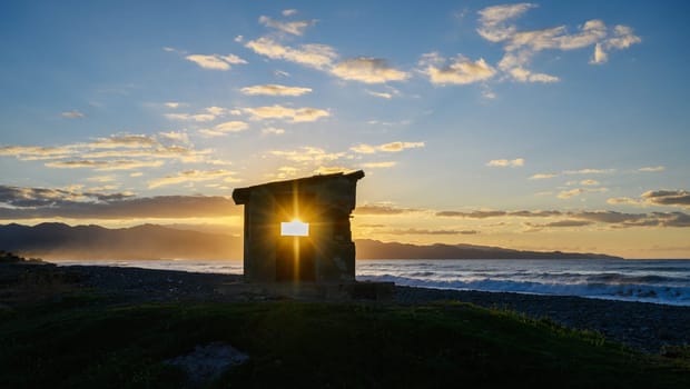 Golden sunlight spills through a crumbling stone wall, highlighting ocean waves at dusk in a picturesque landscape.