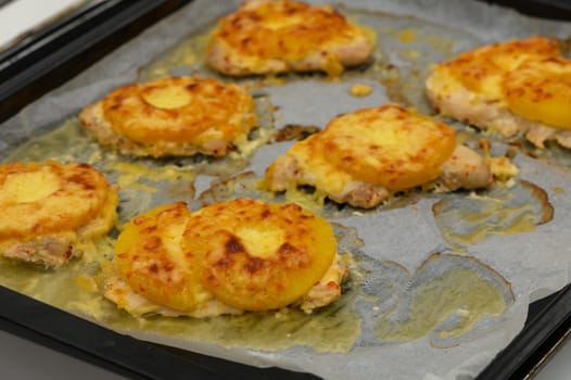 Golden baked chicken pieces with cheese and pineapple are prepared in a warm home kitchen, inviting appetites.