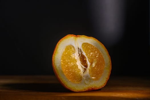 A fresh orange is cut in half, showcasing its juicy segments illuminated by soft, focused light against a dark backdrop.