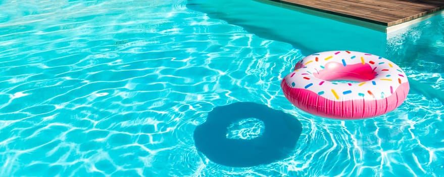 Pink donut inflatable float in turquoise swimming pool with shadow and wooden deck