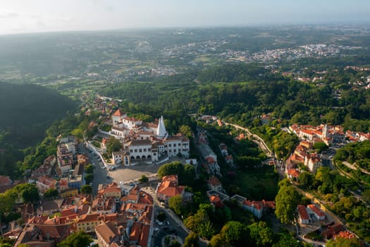 Aerial drone view showcases Sintra National Palace nestled within vast, scenic landscape. The scene captures both the architectural grandeur and natural beauty of this historic site