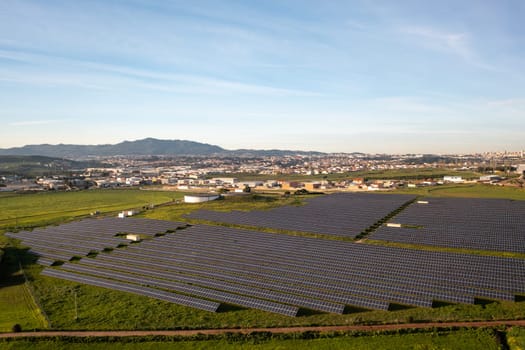 Aerial drone shot of solar panels on agricultural landscape against blue sky. The landscape is fully equipped with green renewable energy generators