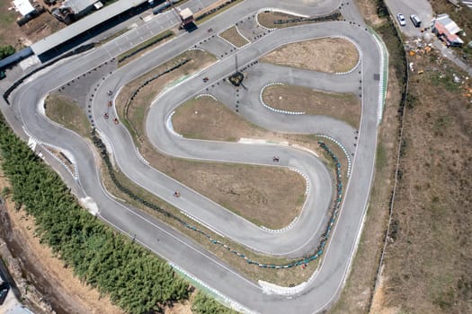 Distant drone capturing go-karts moving on winding racetracks from top aerial perspective. Distant view of racing competition on road at countryside during daytime