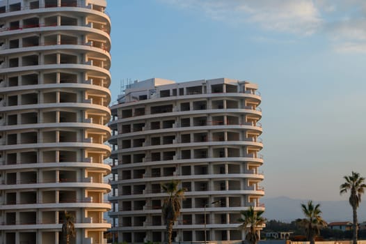 Two unique high-rise buildings rise against a colorful sunset with palm trees swaying gently nearby.