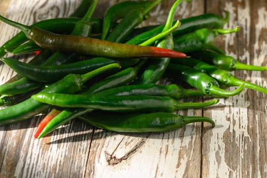 A colorful assortment of fresh green chilies rests on a textured wooden table, illuminated by soft sunlight.