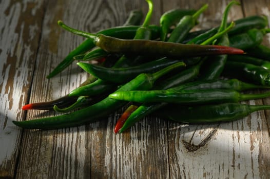 A colorful array of green chili peppers lies on a rustic wooden table, highlighting their rich hue and texture.