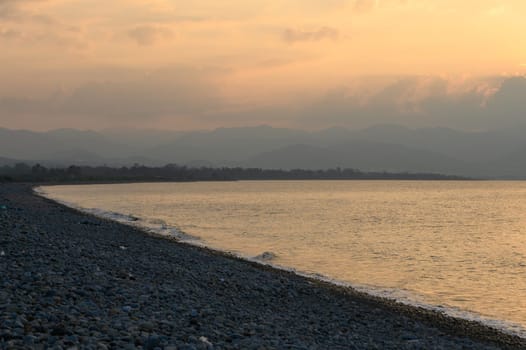 Calm waters reflect the warm hues of sunset, as the shore curves elegantly under a serene sky.