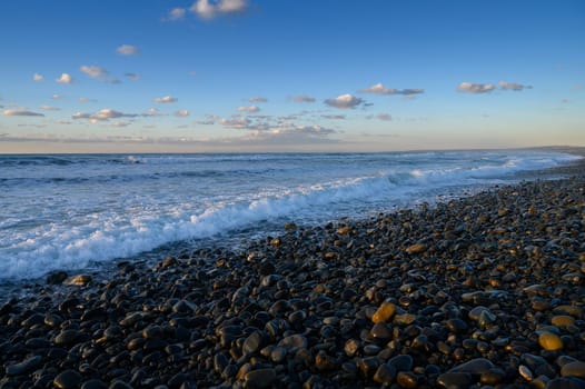 Waves gently crash on a rocky beach while clouds drift across a vibrant sky during the beautiful evening light.