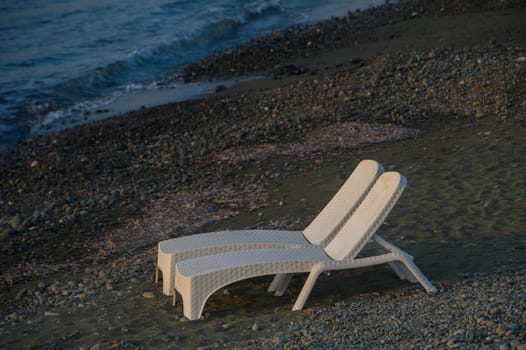 Two white loungers sit peacefully on the shore, overlooking gentle waves at dusk, inviting quiet reflection and calm.