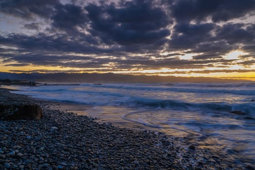 Waves gently crash against the rocky shore as twilight casts a magical glow over the landscape, creating serenity.