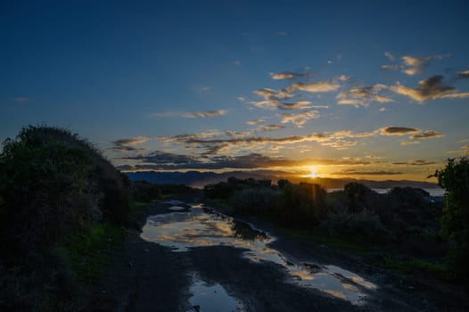 As the sun sets, a tranquil road reflects vibrant colors, inviting exploration through nature's beauty at dusk.