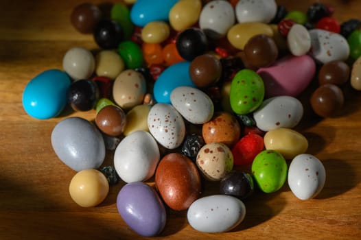 A vibrant collection of assorted candies in various colors and shapes scattered on a warm wooden surface.