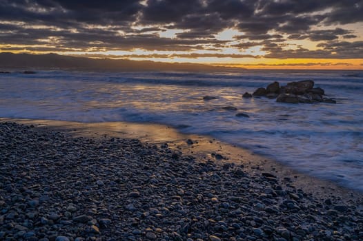 Vibrant colors fill the sky as waves caress the rocky shoreline during a tranquil sunset by the coast.
