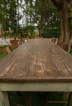 Long rustic table surrounded by wooden chairs, inviting friends for a joyful outdoor meal in nature's embrace.