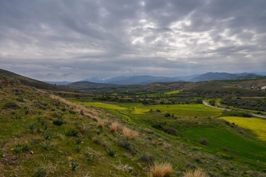 Lush green fields stretch across the valley as storm clouds gather overhead in a tranquil countryside panorama.