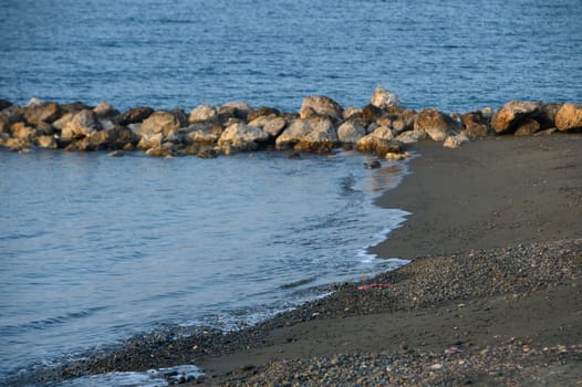 Evening light casts a serene glow on a rocky beach as waves softly kiss the shoreline's edge, inviting peace.