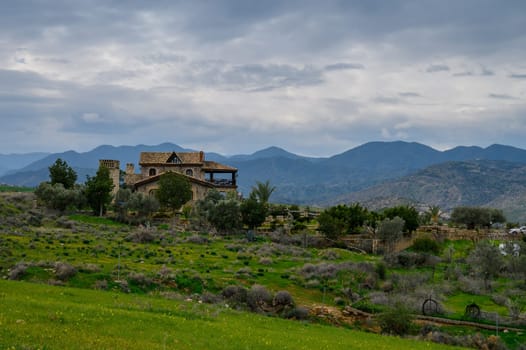 A picturesque view of a charming stone home surrounded by lush greenery and rolling mountains in the distance.